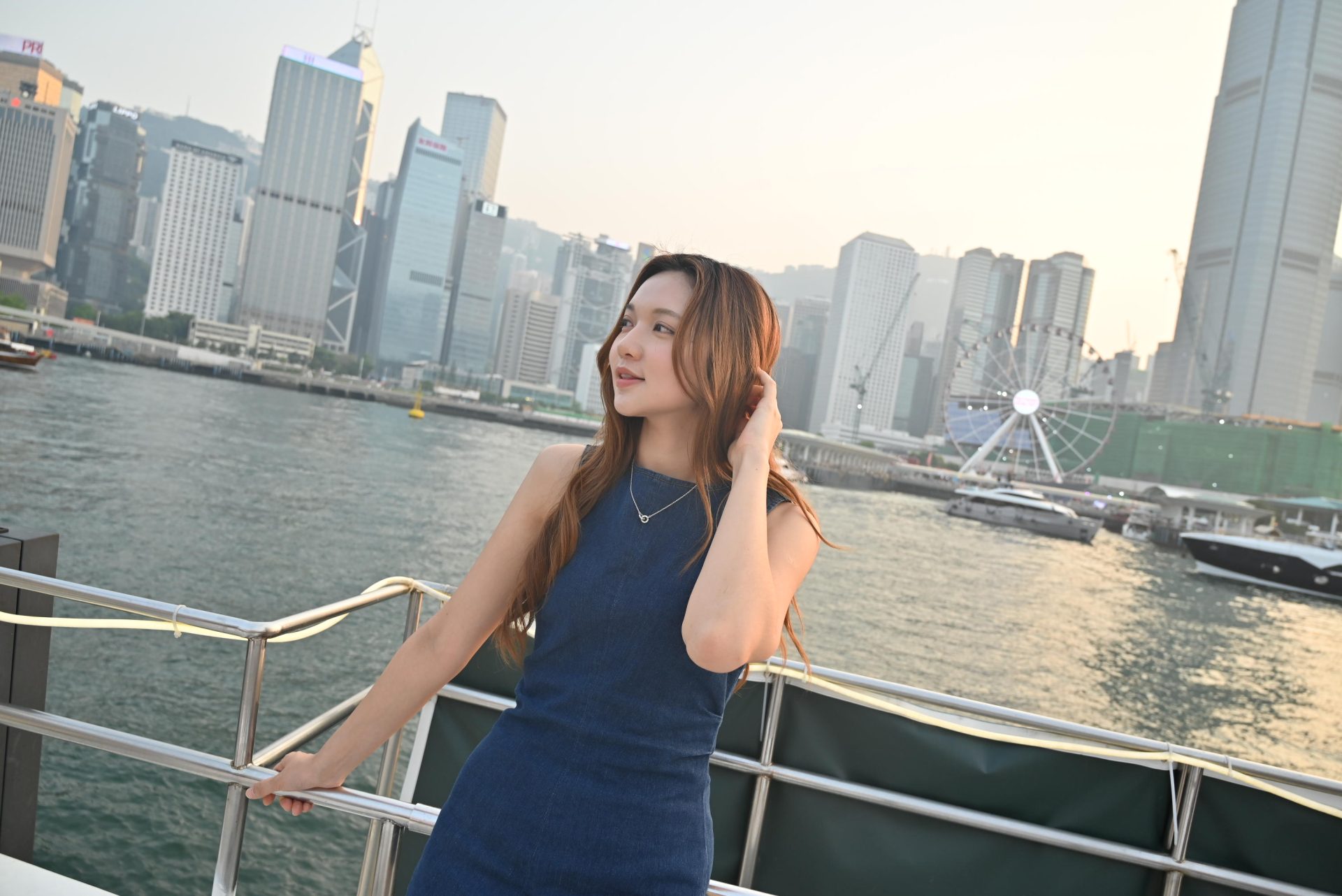 A guest posing on a Dreamer Tours luxury yacht with the Hong Kong Central skyline in the background at sunset.